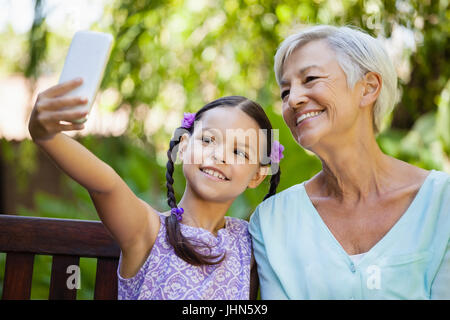 Sorridente ragazza tenendo selfie con nonna al cortile Foto Stock