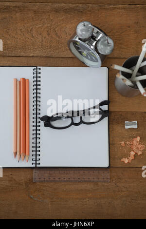 Vista aerea della sveglia, prenota, matita, scala, occhiali e temperino sul tavolo di legno Foto Stock