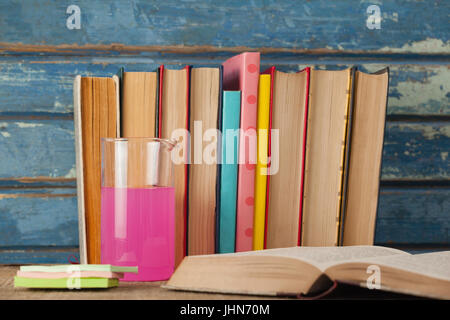 Pila di libri, bicchiere di chimica e sticky notes contro blu sullo sfondo di legno Foto Stock