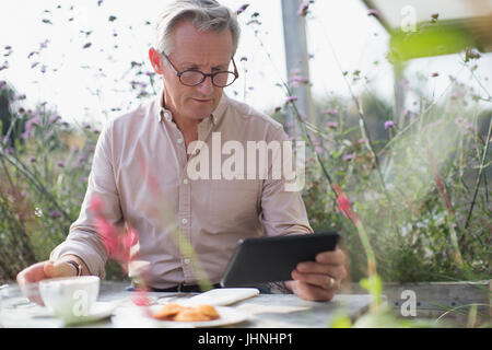 Senior uomo con tavoletta digitale e di bere il caffè al patio tabella Foto Stock