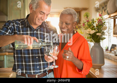 Sorridente coppia senior versando il vino bianco in cucina Foto Stock