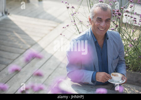 Ritratto sorridente uomo senior di bere il caffè sul patio soleggiato Foto Stock