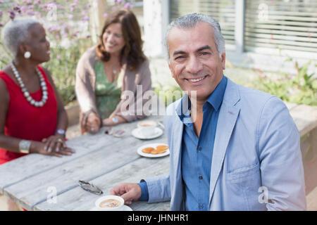 Ritratto sorridente uomo senior di bere il caffè con gli amici al patio tabella Foto Stock