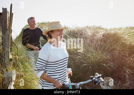 Coppia matura biciclette a piedi lungo la spiaggia soleggiata erba Foto Stock