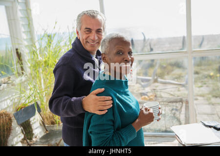 Ritratto sorridente coppia senior avvolgente e di bere il caffè sulla spiaggia soleggiata casa portico di Sun Foto Stock