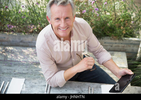 Ritratto sorridente uomo senior con tavoletta digitale sul patio Foto Stock