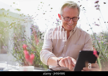Sorridente uomo senior con tavoletta digitale sul patio Foto Stock