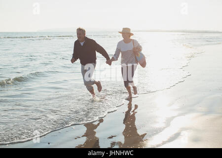 Giocoso Coppia matura tenendo le mani e in esecuzione nella soleggiata ocean surf Foto Stock