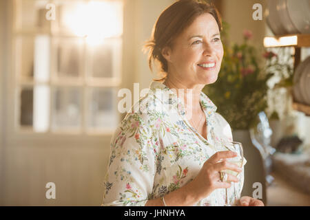 Sorridente donna matura di bere vino in cucina Foto Stock