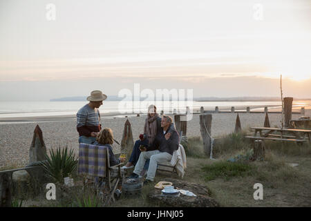 Coppie mature alla brace e bere vino sulla spiaggia al tramonto Foto Stock
