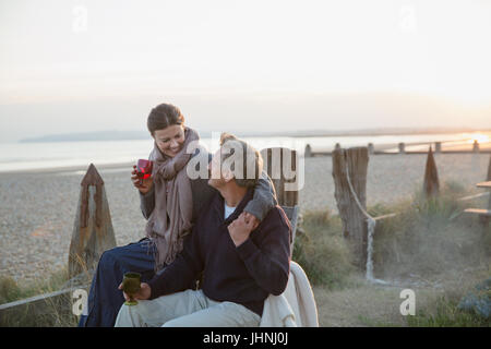 Affettuosa Coppia matura bere vino sulla spiaggia al tramonto Foto Stock