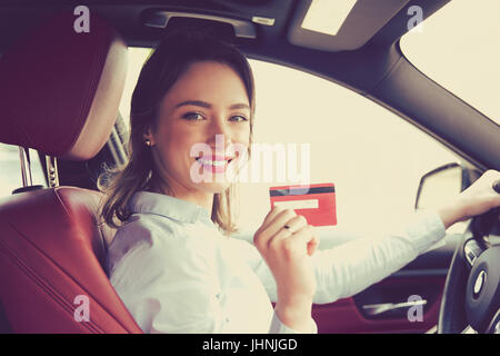 Felice donna seduta dentro la sua nuova vettura che mostra carta di credito Foto Stock