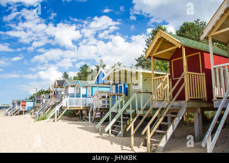 Colorate e cabine in legno su palafitte presso il deserta spiaggia sabbiosa di pozzetti accanto al mare in nirfolk, Regno Unito sotto un cielo blu con un sole estivo. Foto Stock