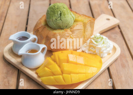 Pane tostato miele tè verde il gelato con maturi barracuda mango e panna montata nella piastra di legno su un tavolo di legno. Foto Stock