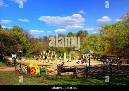 Parco giochi per bambini in un parco verde in maggio con giochi per bambini e genitori Foto Stock