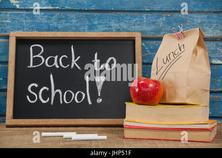 Apple, il pranzo borsa, libri e ardesia con ritorno a scuola contro il testo blu sullo sfondo di legno Foto Stock