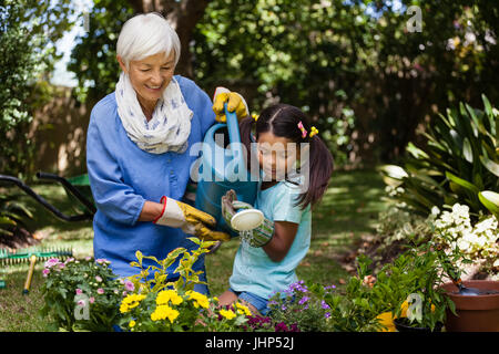 Nonna sorridente e nipote di impianti di irrigazione in cortile Foto Stock