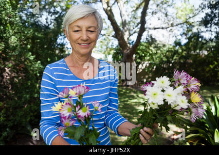 Sorridente donna senior guardando i fiori freschi in cortile Foto Stock