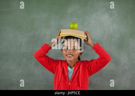 Ritratto di giovane ragazza libri di bilanciamento e di Apple sul suo capo Foto Stock