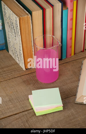 Pila di libri, bicchiere di chimica e sticky notes contro blu sullo sfondo di legno Foto Stock