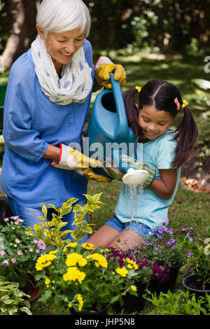 Ragazza sorridente e nonna di impianti di irrigazione in cortile Foto Stock