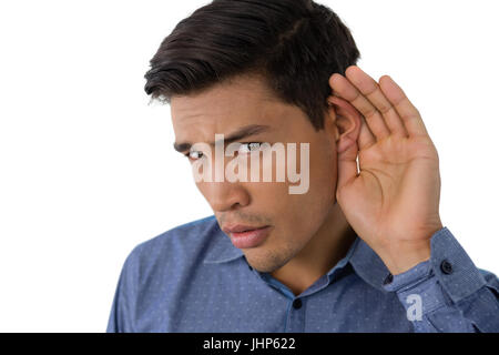 Close up ritratto di imprenditore coppettazione le orecchie mentre in piedi contro uno sfondo bianco Foto Stock