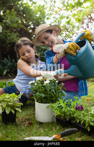 Felice madre con la figlia di irrigazione di piante in vaso mentre è seduto sul campo nel cortile posteriore Foto Stock