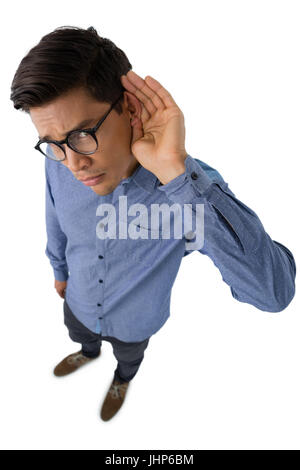 Angolo alto ritratto di imprenditore coppettazione le orecchie mentre in piedi contro uno sfondo bianco Foto Stock