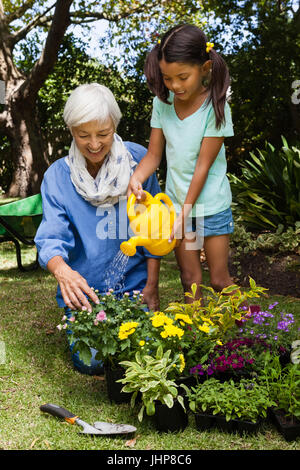 Senior donna che guarda la ragazza di fiori di irrigazione in cortile Foto Stock