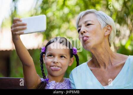 La ragazza e la nonna spuntavano lingua tenendo selfie a backyard Foto Stock