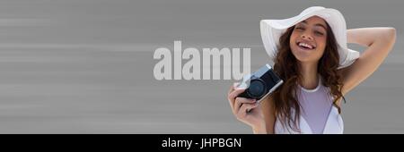 Composito Digitale della donna millenario in estate hat con fotocamera contro sfocato lo sfondo grigio Foto Stock