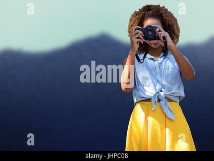 Digital composito della millenaria donna in abiti estivi con fotocamera contro la montagna sfocato Foto Stock