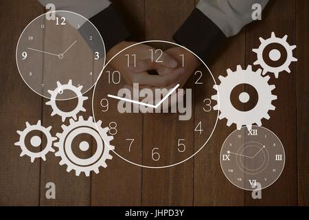 Composito Digitale degli ingranaggi e le icone orologio contro le mani su un tavolo foto Foto Stock