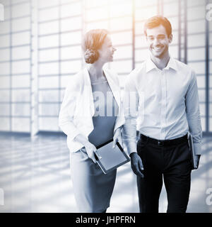 Colleghi di lavoro utilizzando tavoletta digitale mentre si cammina contro la sala bianca con una grande finestra che si affaccia sul city Foto Stock