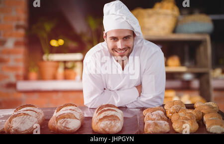 Ritratto di chef maschio in piedi da pane in tavola contro il contatore vuota al coffee shop Foto Stock