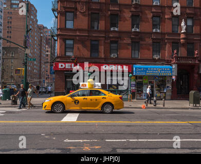 New York , NY USA -- Luglio 12, 2017 -- una cabina è interrotto su 14th street in attesa per la luce a cambiare mentre due pedoni iniziare l'attraversamento della strada Foto Stock