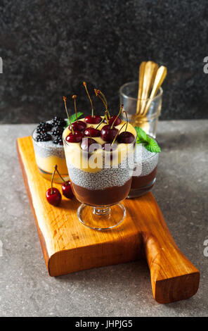 Layered dessert da cioccolato e budino alla vaniglia e anche da chia semi maturi con ciliegie fresche sulla parte superiore e le foglie di menta. Concetto di sano eatin Foto Stock