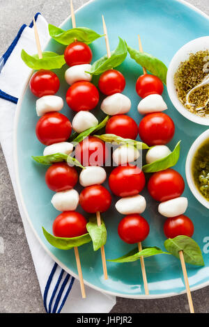 Appetitosi kebab vegetariani da pomodori ciliegia e mini mozzarella in due tipi di basilico e origano sugo come uno snack Foto Stock