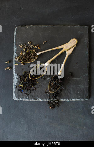 Diversi tipi di tè - verde, nero e tè di frutta con fiori in cucchiai vintage on dark bakcground Foto Stock