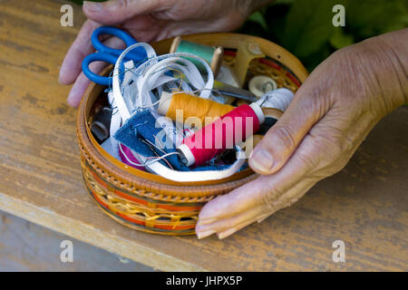 Mani femminili in possesso di una scatola di vimini con filati, aghi e forbici Foto Stock