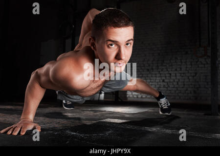 Ritratto di un giovane sportivo facendo spingere ups esercitare con una mano contro un muro di mattoni in palestra per il fitness. Foto Stock