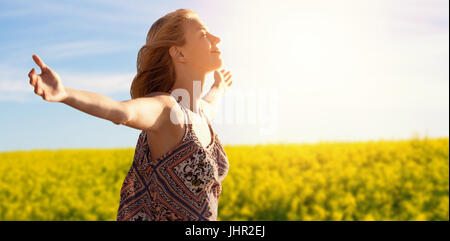 Vista laterale di una donna i bracci di sollevamento fino contro la vista panoramica di giallo senape campo Foto Stock