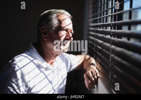 Riflessivo senior paziente di sesso maschile guardando attraverso la finestrella in ospedale Foto Stock