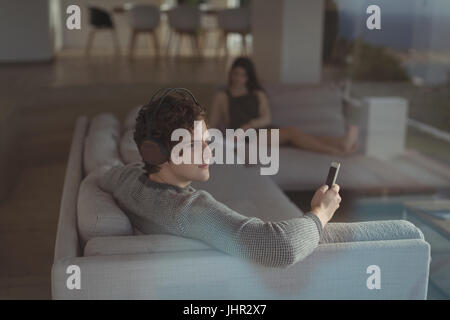 Uomo che ascolta la musica sul telefono cellulare nel salotto di casa Foto Stock