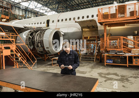 Aeromobili maschio tecnico di manutenzione utilizzando tavoletta digitale presso le compagnie aeree impianto di manutenzione Foto Stock