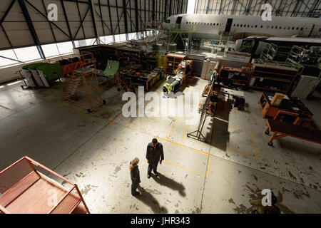 Angolo di alta vista di manutenzione aeromobili ingegneri interagire gli uni con gli altri a compagnie aeree impianto di manutenzione Foto Stock