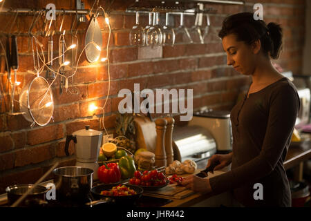 Donna sorridente alla preparazione del cibo mentre in piedi in cucina a casa Foto Stock