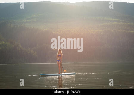 Giovane donna in piedi sul paddleboard nel lago contro la montagna Foto Stock