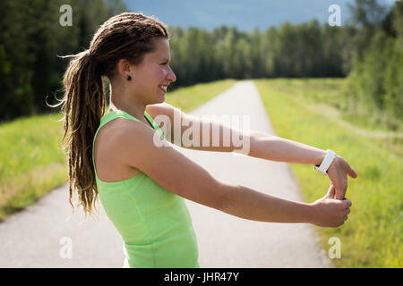 Vista laterale del sorridente giovane donna bracci di estensione sul sentiero Foto Stock