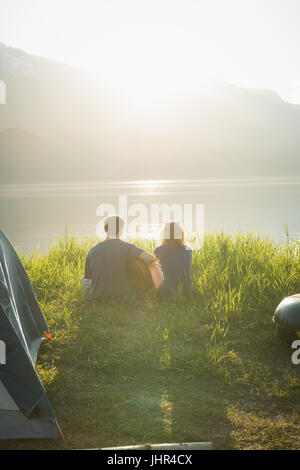Vista posteriore dell'uomo a suonare la chitarra per sua moglie al campeggio Foto Stock